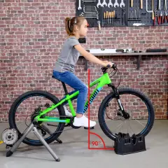 Ein Mädchen sitzt auf einem grünen Kinderfahrrad, das auf einem Rollentrainer steht. Eine rote Linie zeigt den 90-Grad-Winkel für das richtige Einstellen des Kinderfahrrads.