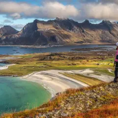 Wanderer blickt auf malerische Küste mit Bergen. Die Lofoten zeigen sich von ihrer besten Reisezeit-Seite.