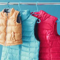 Drei Steppwesten in Orange, Türkis und Pink hängen an Kleiderbügeln. So waschen Sie Ihre daunenjacke waschen ohne trockner.