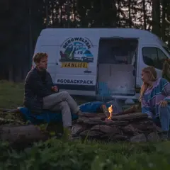 Ein Paar genießt das Lagerfeuer beim wildcampen Bayern. Ihr Van steht im Hintergrund, bereit für das nächste Abenteuer.