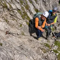 Vier Wanderer genießen den **Mindelheimer Klettersteig**. Ein Stahlseil sichert den Weg über felsiges Gelände.