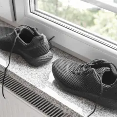 Schwarze Turnschuhe trocknen auf einem Fensterbrett über einer Heizung.