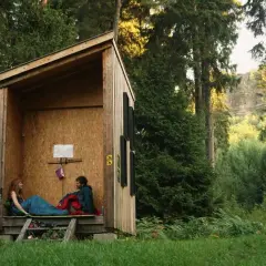 Ein Paar entspannt in einer Schutzhütte im Wald. Hier darf man im Wald schlafen und die Natur genießen.
