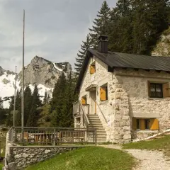 Steinernes Haus mit Holzterrasse und Bergkulisse im Tannheimer Tal. Ein Geheimtipp für Wanderer.