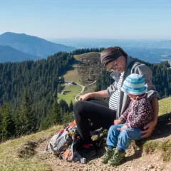 Schwangerschaft und Wandern: Eine Frau mit Babybauch und Kind genießen die Aussicht auf Berge und Wälder.