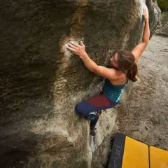 Eine Frau klettert an einem Felsen in Fontainebleau. Sie nutzt ihre Kraft und Technik beim Bouldern.