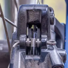 Nahaufnahme einer Fahrradbremse. Die Bremsbeläge schleifen einseitig am Rotor. Staub und Schmutz sind sichtbar.