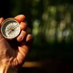 Eine Hand hält einen goldenen Kompass, der die Himmelsrichtungen anzeigt. So lernt man, wie liest man einen Kompass.