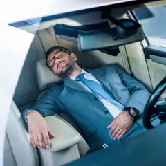 Ein Geschäftsmann im Anzug schläft im Auto. Ob man in Italien im Auto schlafen darf, ist eine andere Frage.
