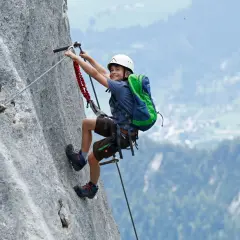 Ein Junge mit Rucksack und Helm meistert einen Klettersteig. Ein tolles Abenteuer für klettersteig kinder!