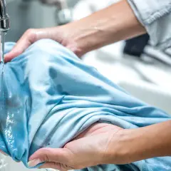 Hände spülen Matsch aus Kleidung unter fließendem Wasser.