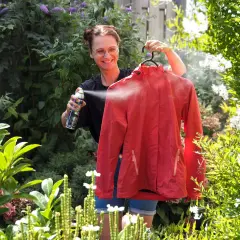 Frau sprüht rote Softshelljacke im Garten ein, um sie zu waschen und zu imprägnieren.