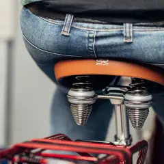 Person sitzt auf einem Fahrradsattel. Der Sattel ist braun und hat Federn. Der Sattel zu breit für Komfort.