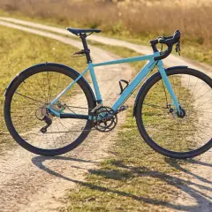 Ein hellblaues Fahrrad mit Schutzblechen steht auf einem Feldweg. Der Unterschied zwischen Cyclocross und Gravel wird hier deutlich: Dieses Rad ist bereit für Abenteuer auf Schotterwegen.