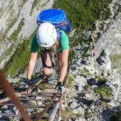 Bergsteigerin klettert eine Leiter hinauf. Die Klettersteige haben unterschiedliche Schwierigkeitsgrade, diese hier scheint mittelschwer zu sein.