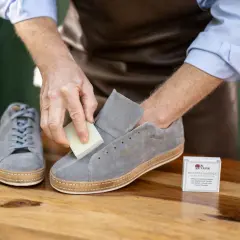 Mann reinigt graue Nubukleder-Sneaker mit einem speziellen Radierer.