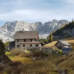 Steinhäuser und Holzhütten am Fuße eines majestätischen, schneebedeckten totes Gebirge. Herbstliche Bäume leuchten golden.
