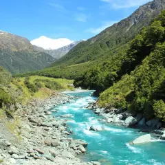 Türkisfarbener Fluss schlängelt sich durch ein Tal mit bewaldeten Hängen und schneebedeckten Gipfeln, die an Roy's Peak erinnern.
