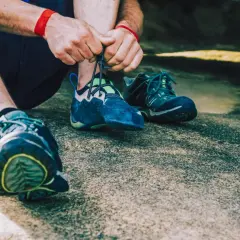 Hände schnüren blaue Kletterschuhe, bereit für den nächsten Aufstieg. Die Füße sind für das Klettern vorbereitet, um die Felsen zu meistern.