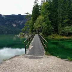 Ein schmaler Steg führt über das smaragdgrüne Wasser des Eibsees. Der eibsee rundweg lädt zu einer Erkundung der malerischen Natur ein, umgeben von dichten Wäldern und Bergen.