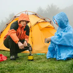 Zwei Camper im Regen bereiten sich eine warme Mahlzeit zu, während das Zelt trocknen muss.