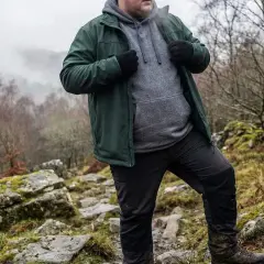 Mann in grüner Jacke und grauer Kapuzenjacke wandert durch felsiges Gelände. Die Jacke ist softshell wasserdicht und schützt vor dem Wetter.