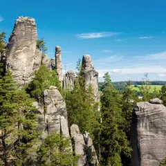 Felsformationen in Tschechien, ideal zum Klettern, umgeben von grünen Bäumen und einem blauen Himmel.