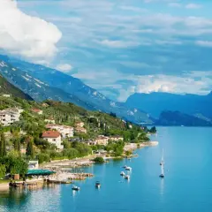 Ein malerisches Dorf am Gardasee in Norditalien, mit Häusern, die sich an den grünen Hang schmiegen, und dem tiefblauen Wasser, das zum Segeln einlädt.