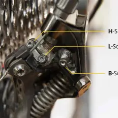 Nahaufnahme eines Fahrrad-Schaltwerks, das zeigt, wie man das Shimano Deore einstellt. H-, L- und B-Schrauben sind markiert.