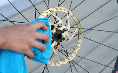 Hand reinigt goldene Fahrrad-Scheibenbremse mit blauem Tuch. Perfekt für den Wechsel der Scheibenbremse am Fahrrad.