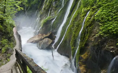 Ein Pfad führt entlang einer tosenden Klamm in Bayern, wo Wasserfälle über moosbewachsene Felsen stürzen.