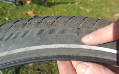 Finger zeigt auf abgefahrenen Fahrradreifen mit der Aufschrift "ROTATION". Zeit, wann Fahrradreifen wechseln.