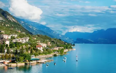 Ein malerisches Dorf am Gardasee in Norditalien, mit Häusern, die sich an den grünen Hang schmiegen, und dem tiefblauen Wasser, das zum Segeln einlädt.