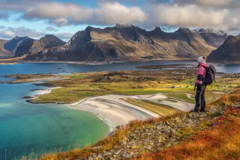 Wanderer blickt auf malerische Küste mit Bergen. Die Lofoten zeigen sich von ihrer besten Reisezeit-Seite.