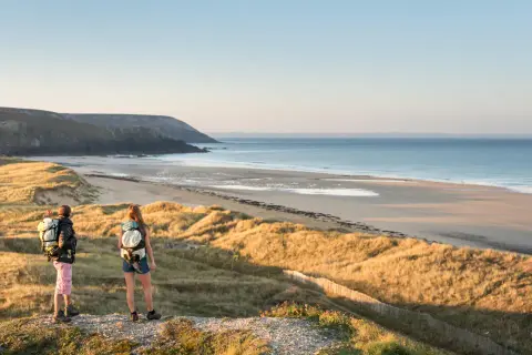 Zwei Wanderer mit Rucksäcken genießen den Ausblick auf die Küste der Bretagne.