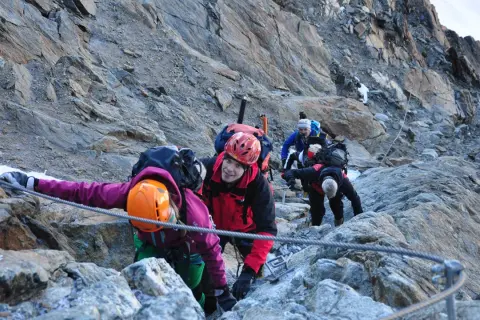 Bergsteiger seilen sich auf dem Weg zur Wildspitze ab. Ein Mann im roten Anzug lächelt in die Kamera.