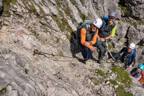 Vier Wanderer genießen den **Mindelheimer Klettersteig**. Ein Stahlseil sichert den Weg über felsiges Gelände.