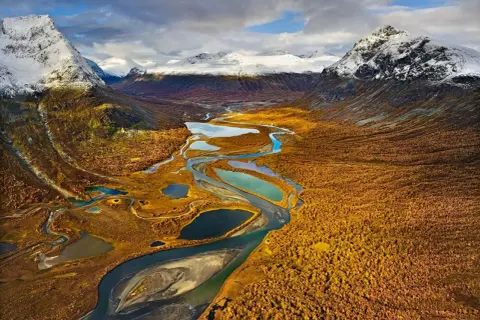 Herbstliche Landschaft mit Flüssen und Seen, ideal für fernwanderwege schweden. Schneebedeckte Berge im Hintergrund.