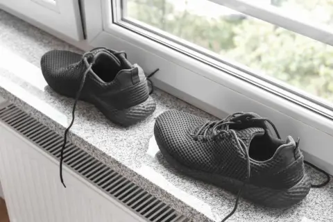 Schwarze Turnschuhe trocknen auf einem Fensterbrett über einer Heizung.