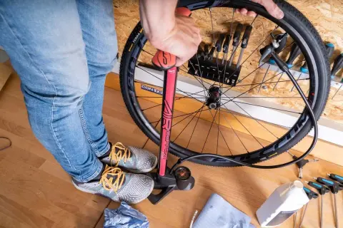 Fahrradreifen aufpumpen mit einer roten Luftpumpe. Werkzeug und eine Flasche Flüssigkeit liegen bereit.