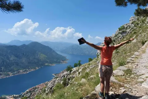 Frau genießt die Aussicht beim **Montenegro wandern**. Der Blick schweift über die Bucht von Kotor, umgeben von Bergen.
