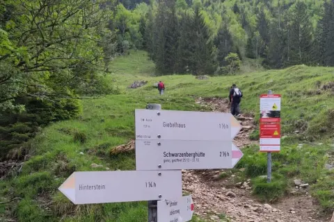 Wegweiser für eine Schrecksee Wanderung: Giebelhaus, Schwarzenberghütte und Hinterstein sind Ziele. Wanderer steigen bergauf.