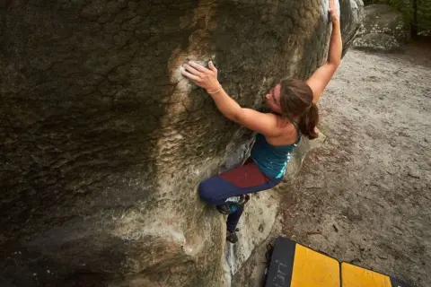 Eine Frau klettert an einem Felsen in Fontainebleau. Sie nutzt ihre Kraft und Technik beim Bouldern.