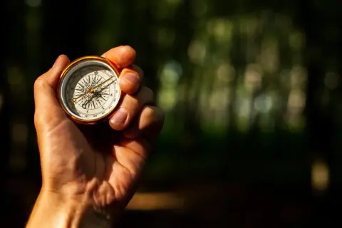 Eine Hand hält einen goldenen Kompass, der die Himmelsrichtungen anzeigt. So lernt man, wie liest man einen Kompass.