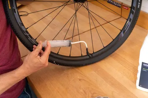 Mit einer Spritze wird Dichtmilch in den Fahrradreifen gefüllt, um die Laufrichtung zu optimieren und Pannen zu vermeiden.
