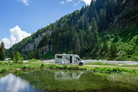 Wohnmobil am Bergsee. Hier darf man in der Schweiz wild campen, umgeben von grünen Hängen und Nadelbäumen.