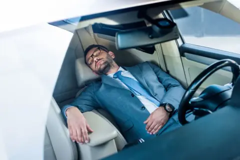 Ein Geschäftsmann im Anzug schläft im Auto. Ob man in Italien im Auto schlafen darf, ist eine andere Frage.