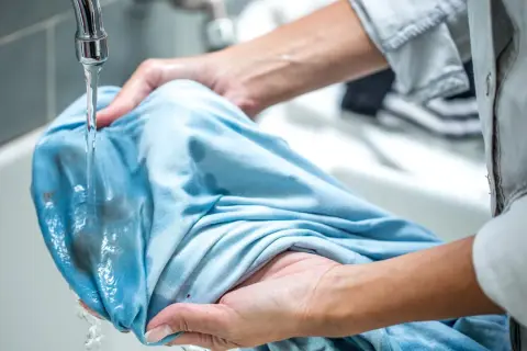 Hände spülen Matsch aus Kleidung unter fließendem Wasser.
