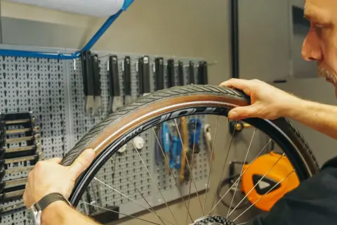 Mann wechselt den Fahrradschlauch. Werkzeugwand im Hintergrund.