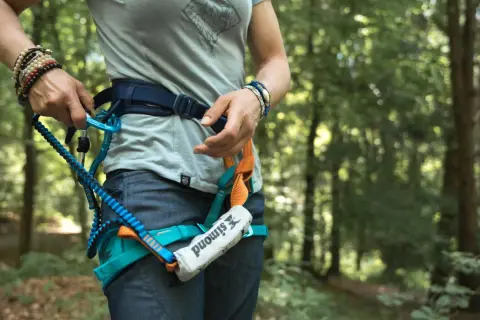 Person legt Klettersteigset an. Sicherungsgurt mit Karabiner und Seil im Wald.